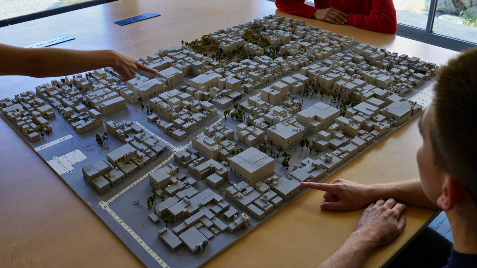 Planners around a table pointing at a physical scale model of a settlement plan.